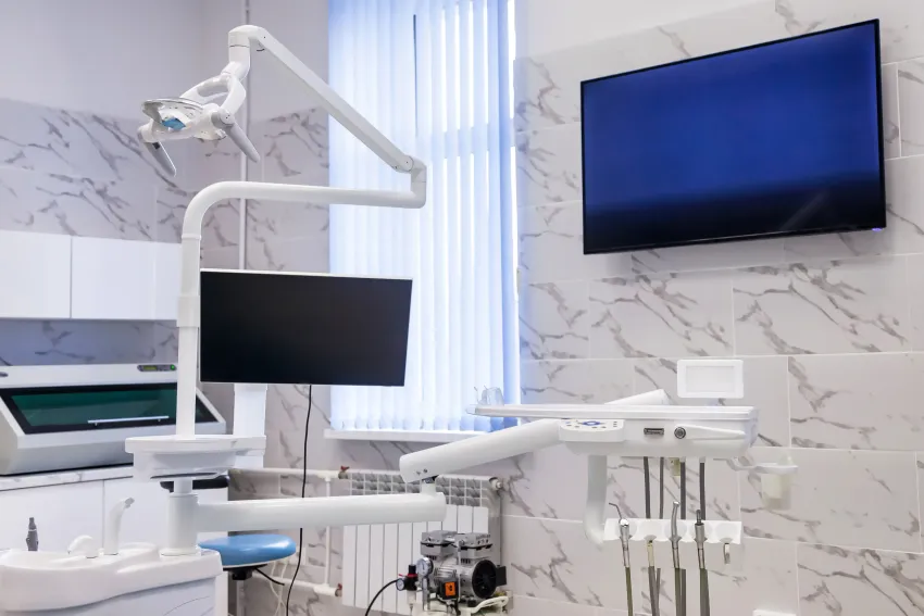 Modern dental exam room with white equipment, monitors, and a wall-mounted TV