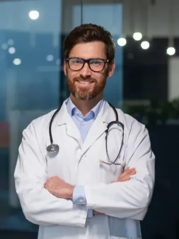 A doctor with a stethoscope around his neck is standing with his arms crossed.