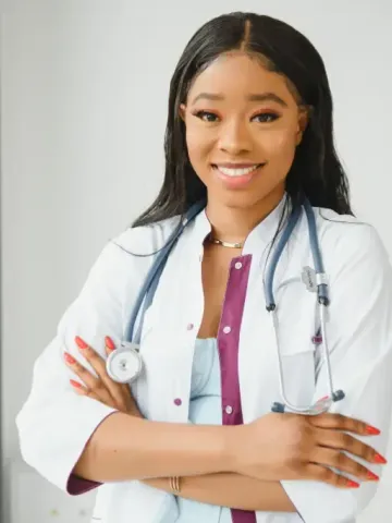 A woman in a lab coat with a stethoscope around her neck is smiling.