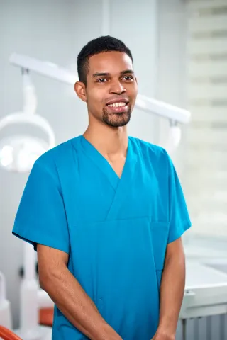 A man in a blue scrub is standing in a dental office.