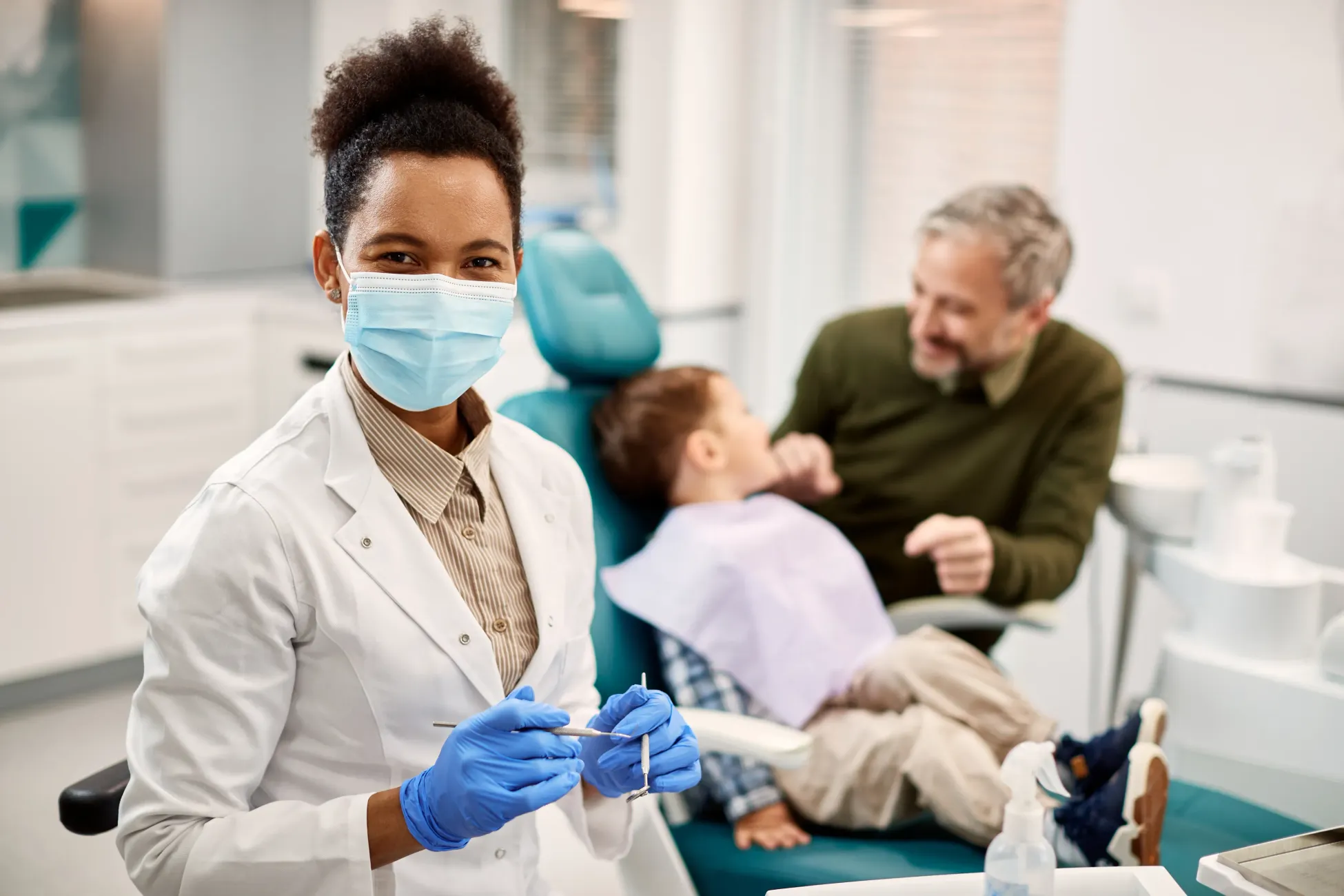 A female dentist is holding a syringe in front of a child in a dental chair.