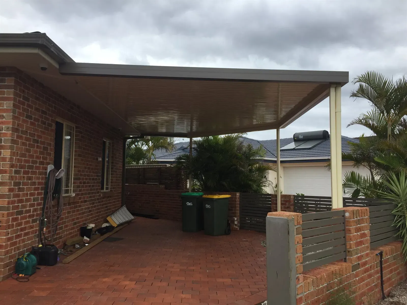A brick house with a carport and trash cans in front of it — Hunter & Mid Coast Patios In Forster-Tuncurry, NSW