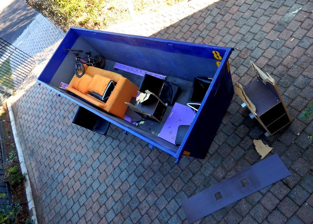 A Blue Dumpster Filled With Furniture and a Bicycle — Gardners Yamba Skip Bin Hire in Yamba, NSW