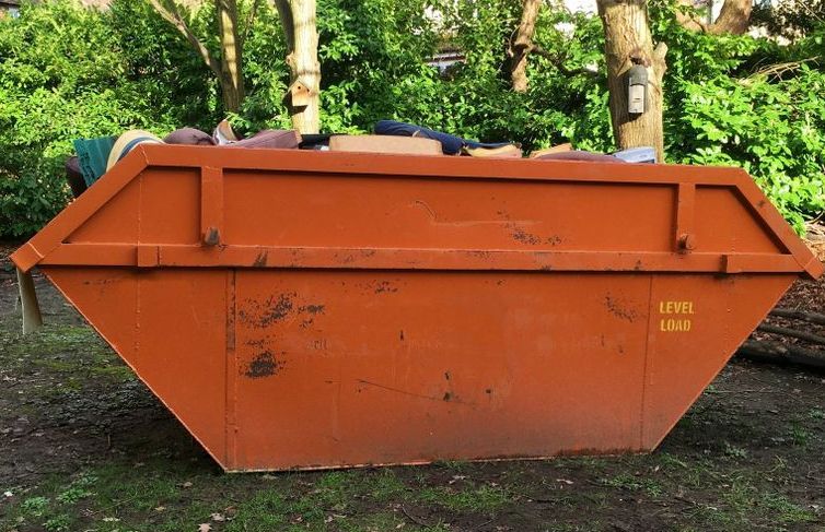 A Large Orange Dumpster is Sitting in the Grass — Gardners Yamba Skip Bin Hire in Grafton, NSW