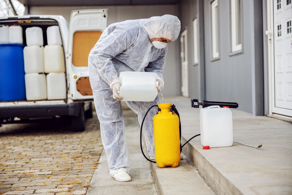 A Man in a Protective Suit is Spraying Chemicals on the Sidewalk — Gardners Yamba Skip Bin Hire in Townsend, NSW
