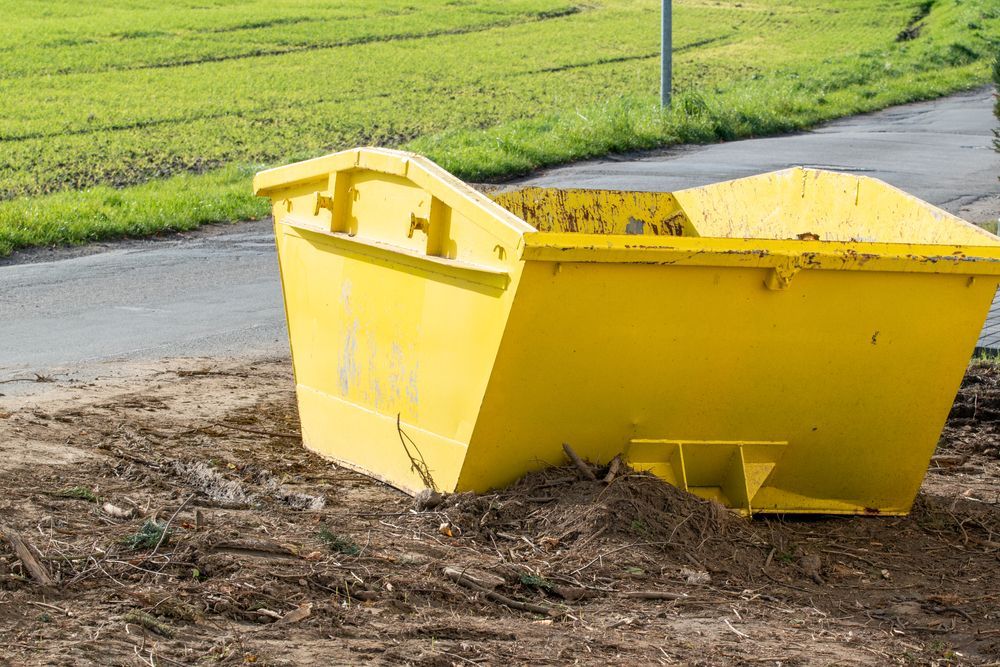 A Yellow Dumpster is Sitting on Top of a Dirt Field Next to a Road — Gardners Yamba Skip Bin Hire in Maclean, NSW