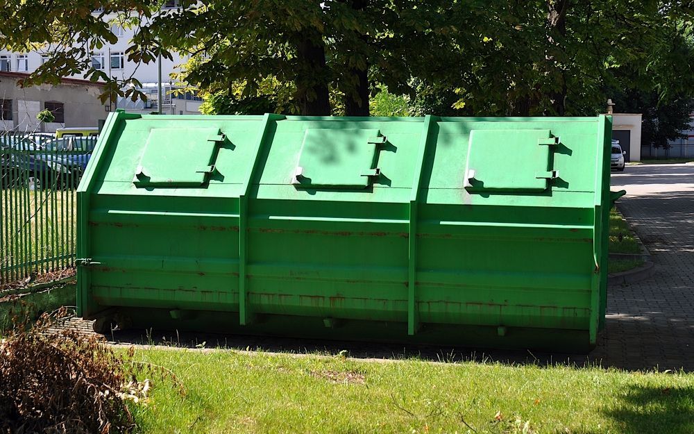 A Green Dumpster is Sitting in the Grass Next to a Fence — Gardners Yamba Skip Bin Hire in Yamba, NSW