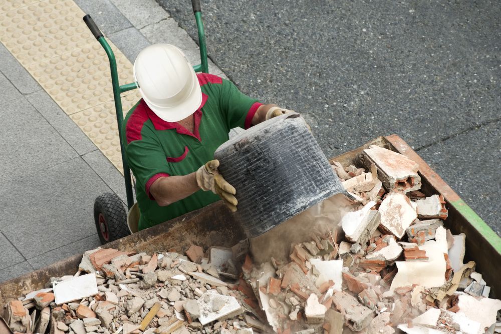 A Man Wearing a Hard Hat is Loading Bricks Into a Dumpster — Gardners Yamba Skip Bin Hire in Townsend, NSW