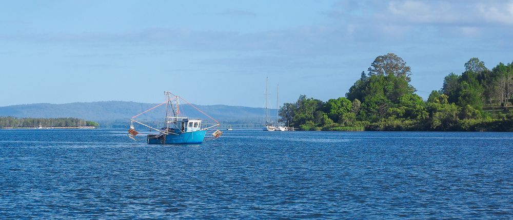 A Blue Boat is Floating on Top of a Large Body of Water — Gardners Yamba Skip Bin Hire in Maclean, NSW