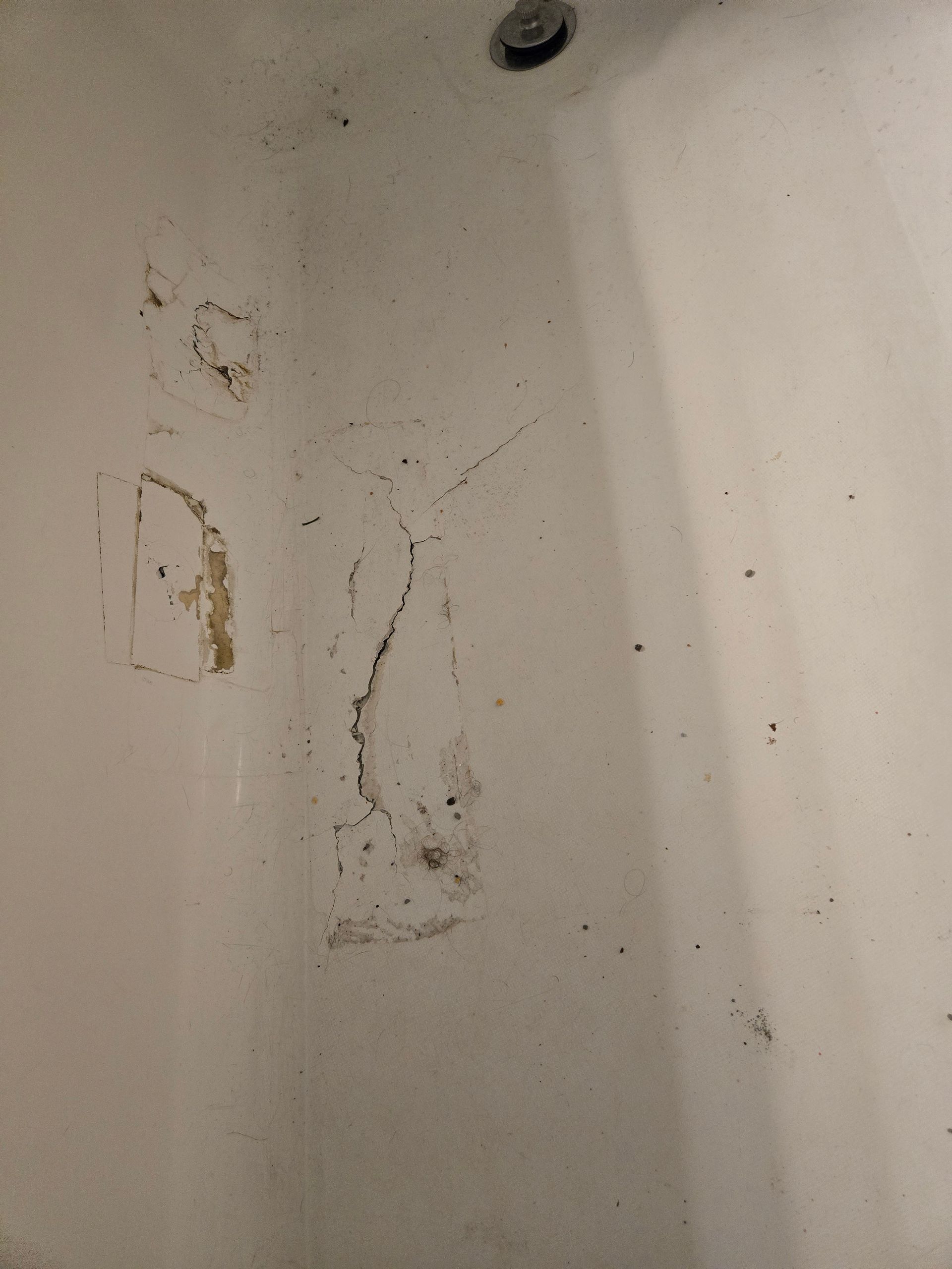 Dirty white shower or bathtub corner with stains and mold spots on the wall.