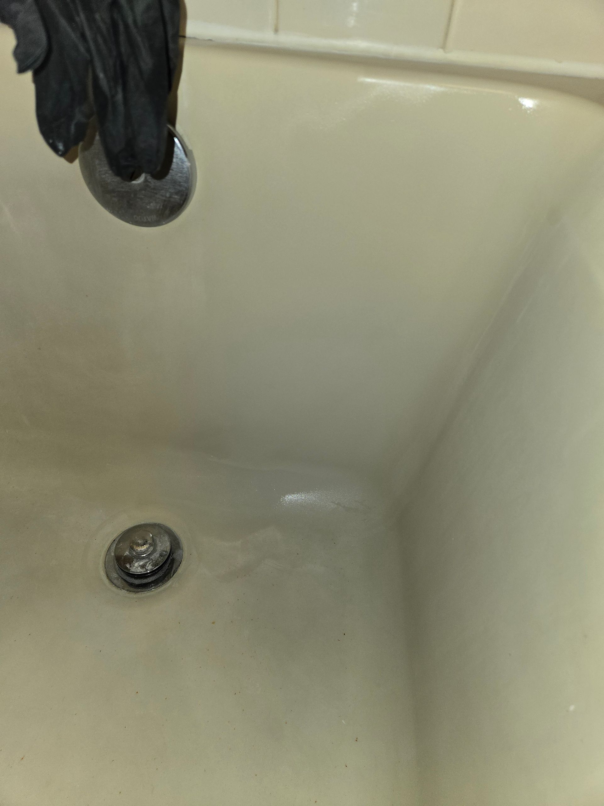 Bathtub with a dark glove near the drain and a small round drain stopper.