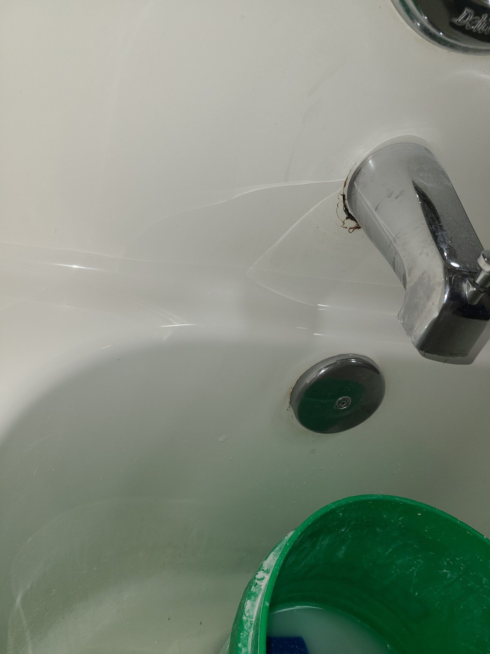 White sink with chrome faucet and green cup, showing a small water leak or drip stain near the tap