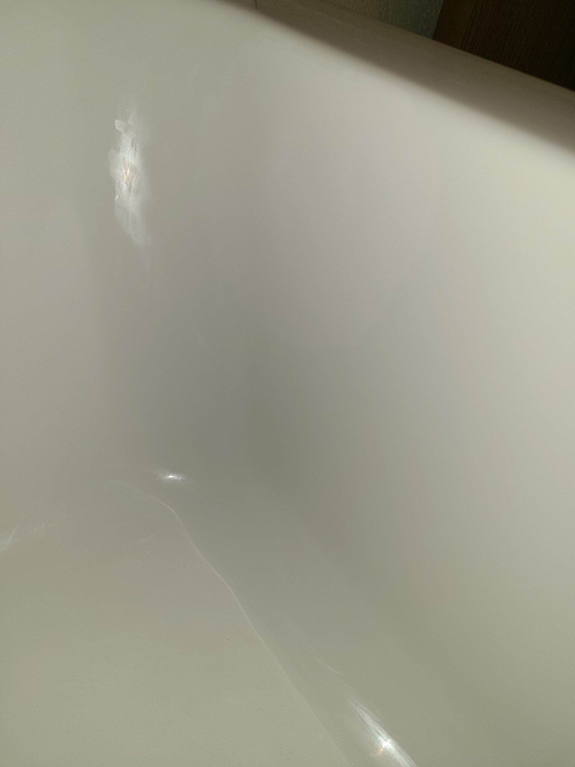 Close-up of a glossy white ceramic surface with a small bright reflection of light.