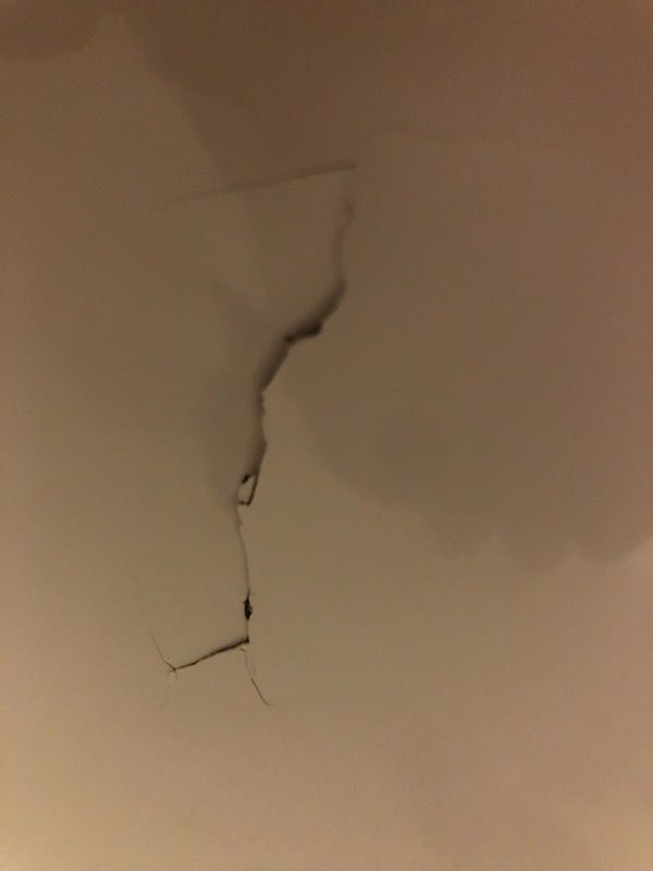Cracked beige wall with a vertical split and peeling plaster near the ceiling