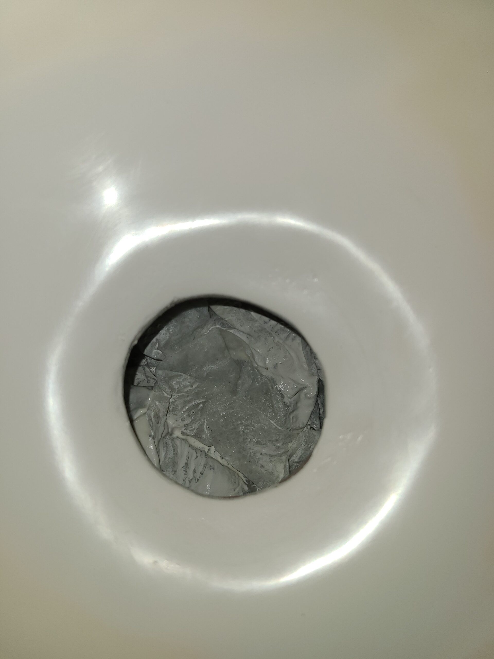 Close-up of a sink drain with a gray metal strainer in a white basin.