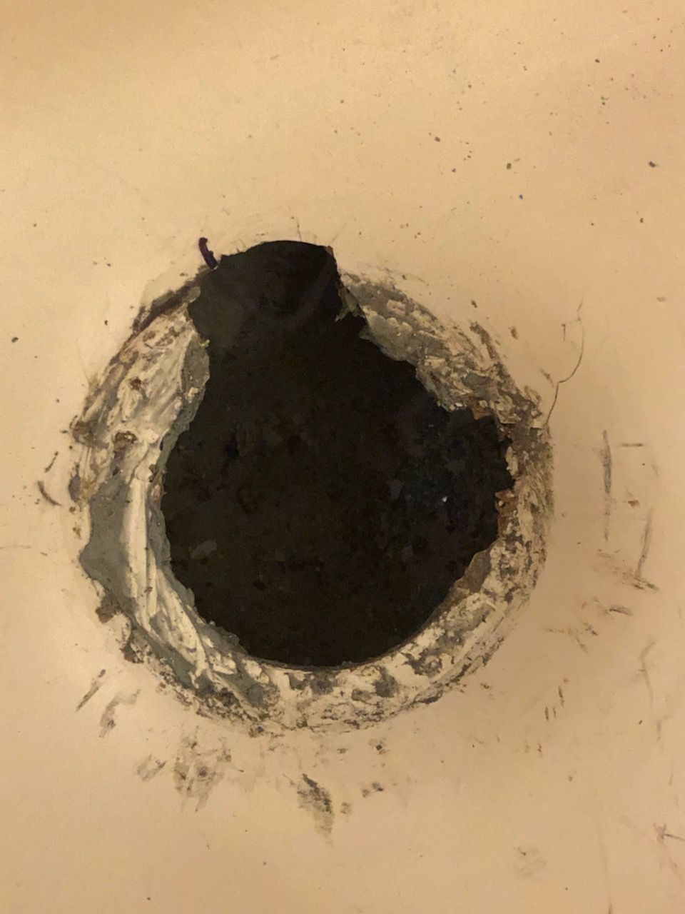 Close-up of a rough circular hole in a beige wall, with dark empty center and chipped edges