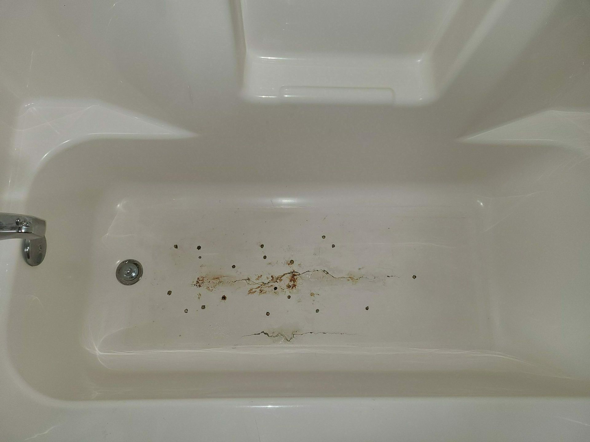 Dirty white bathtub with scattered debris and stains near the drain