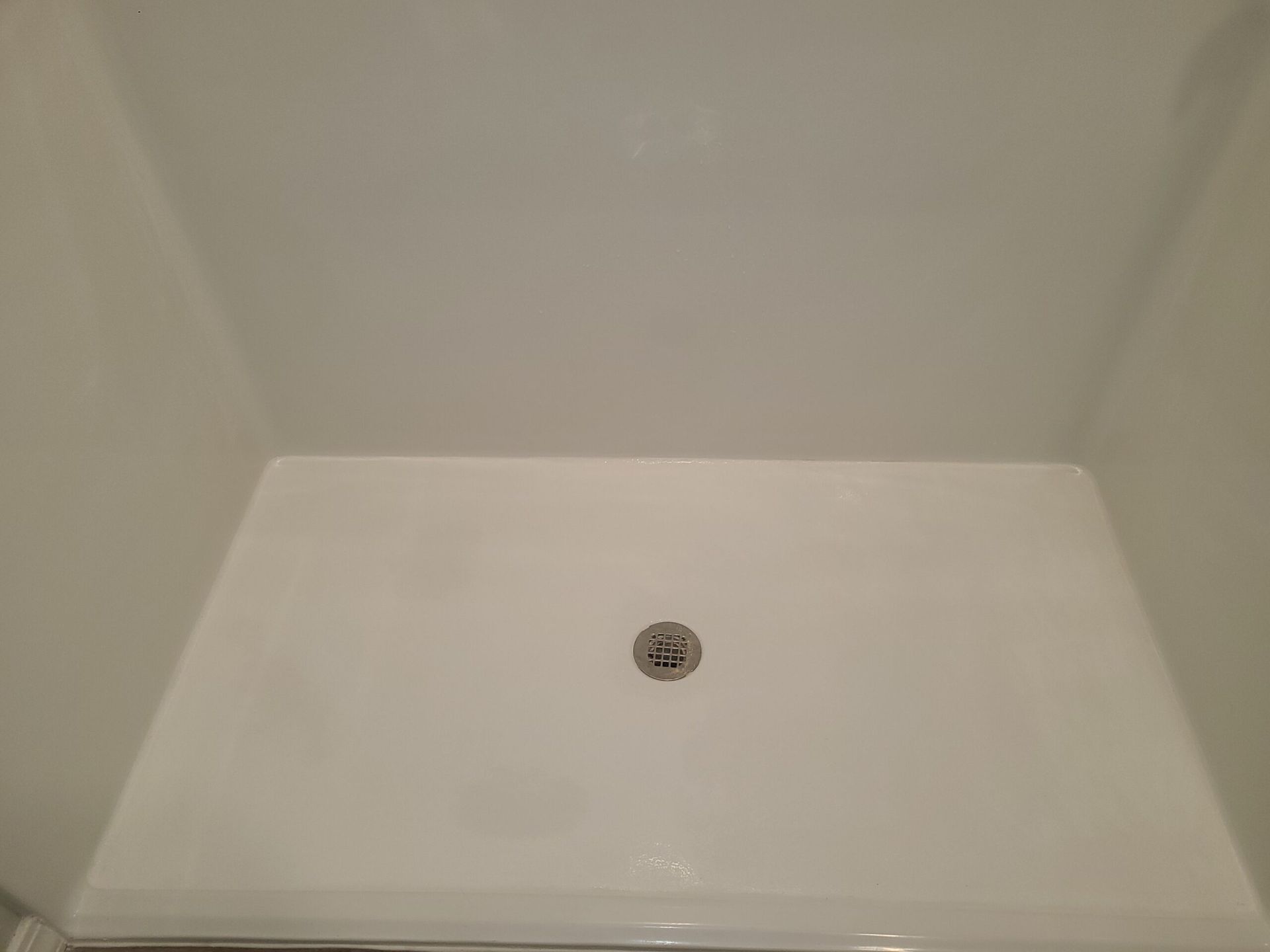 Empty white shower stall with a centered drain.