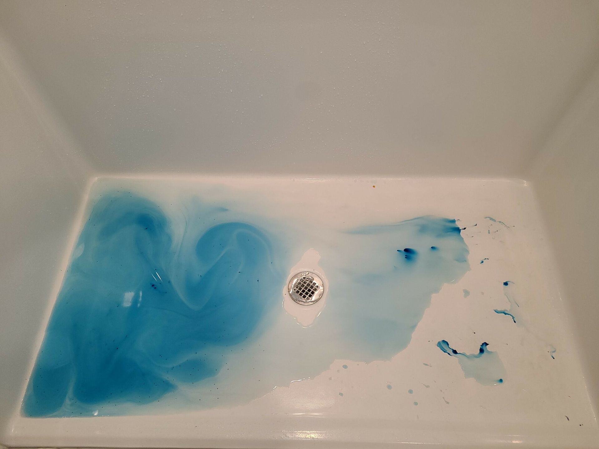 White sink basin with blue liquid swirled across the bottom and a drain in the center