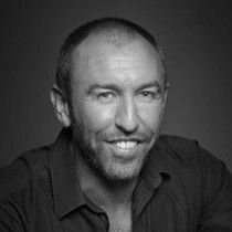 A man with a beard is smiling in a black and white photo.
