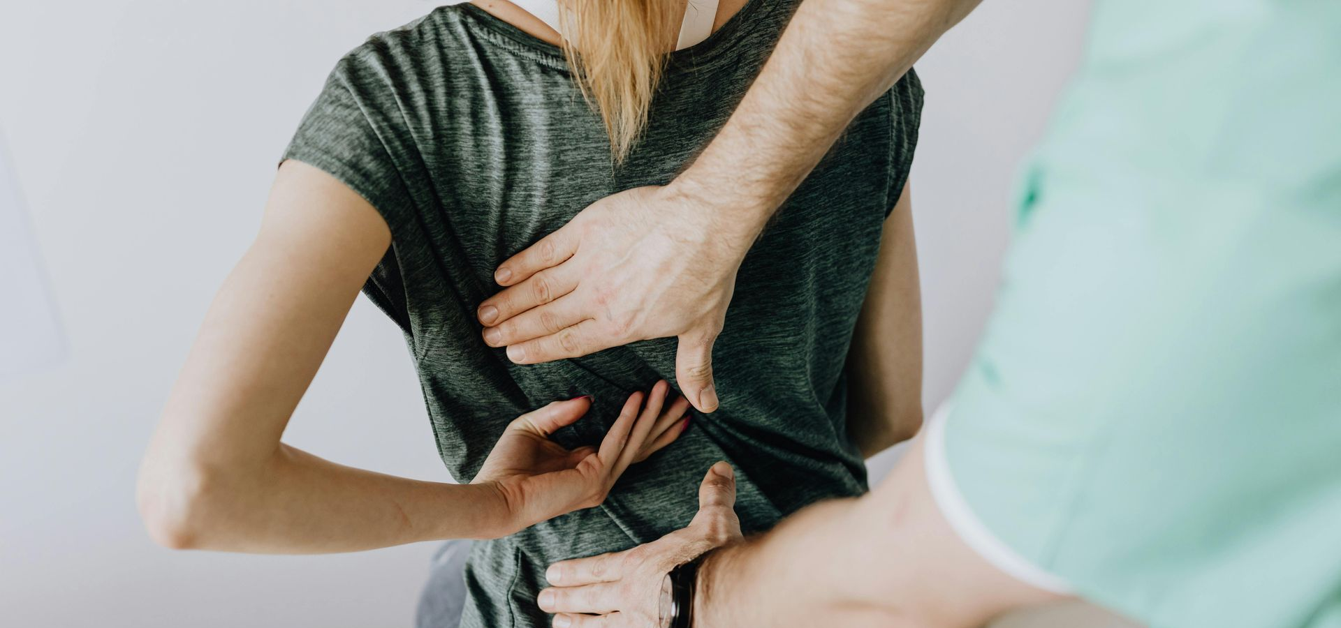 A person being examined for back pain by a healthcare provider. Hands are on the person's back.