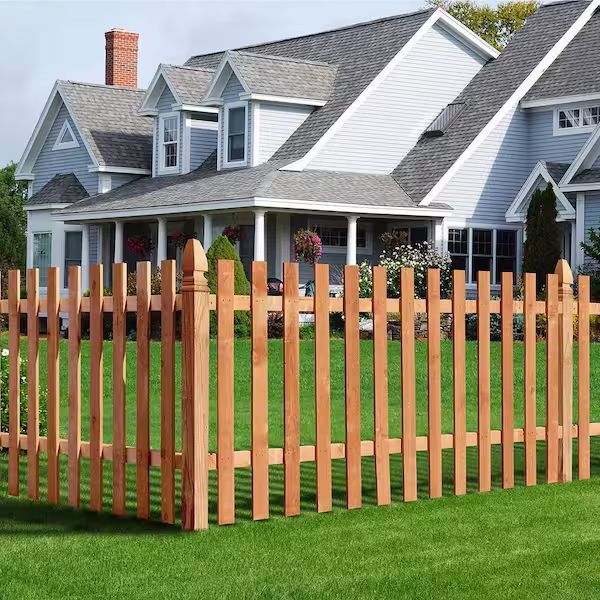 A wooden picket fence stands in front of a blue two-story house with a grey roof and front porch.