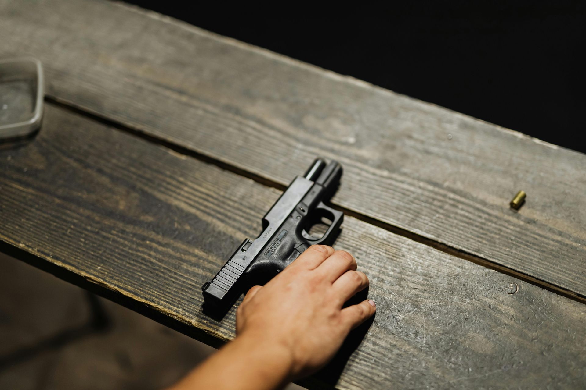 Hand reaching for a handgun on a wooden surface; bullet nearby.
