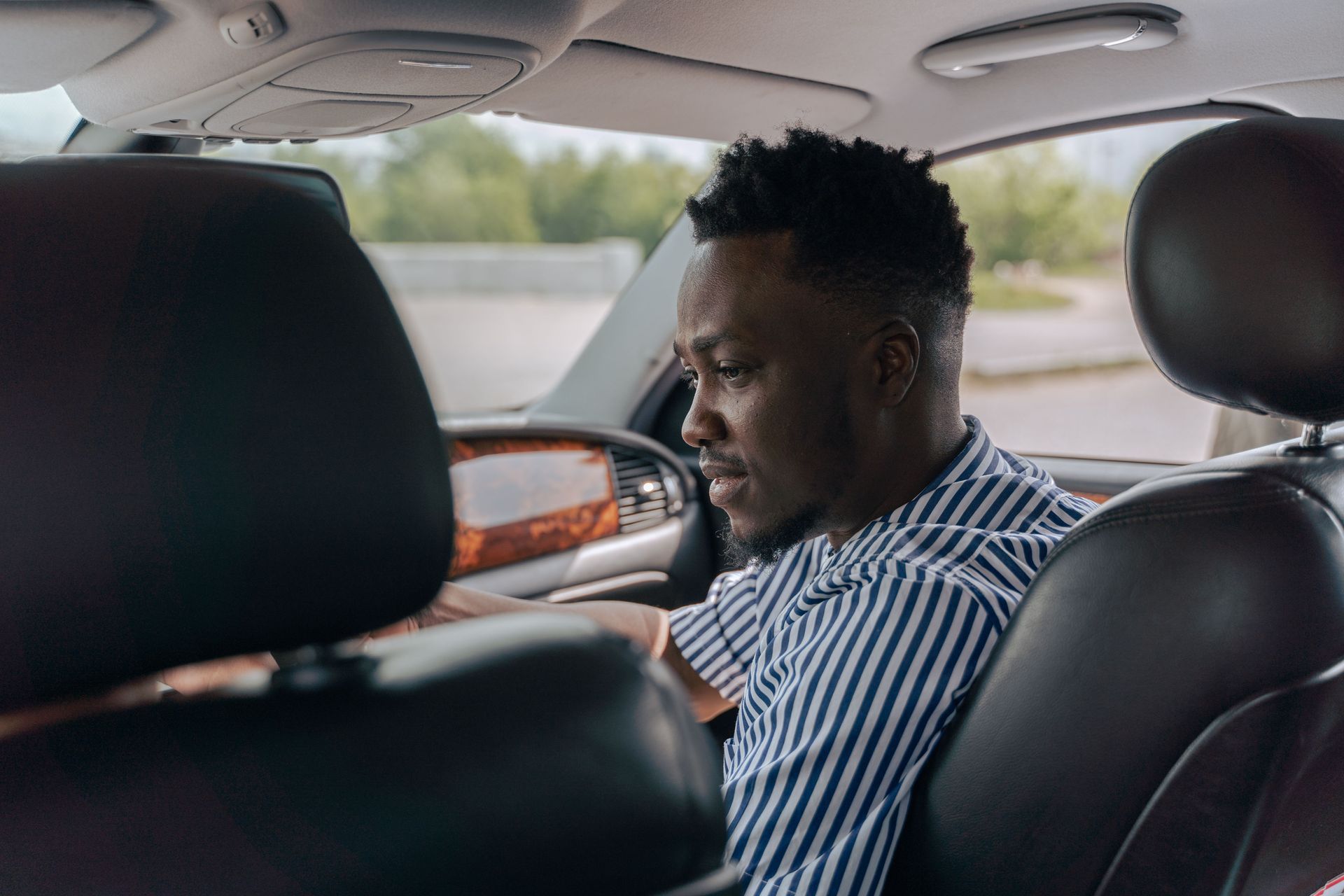 Person sitting in the back seat of a car, looking down, with black leather seats and a striped shirt