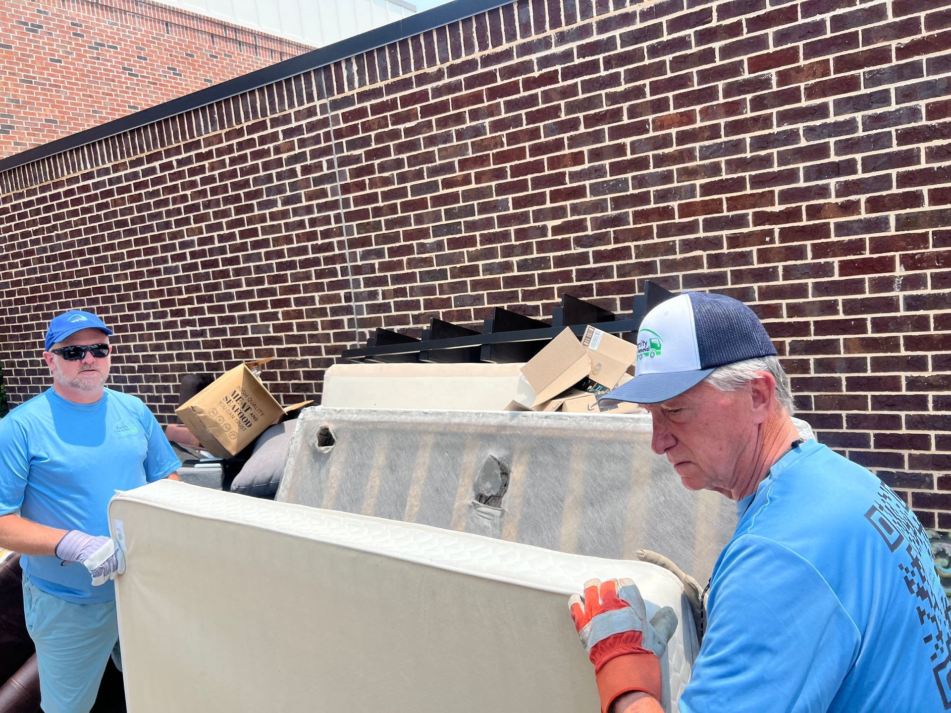 A pile of mattresses and carpet on a sidewalk in front of a brick building.