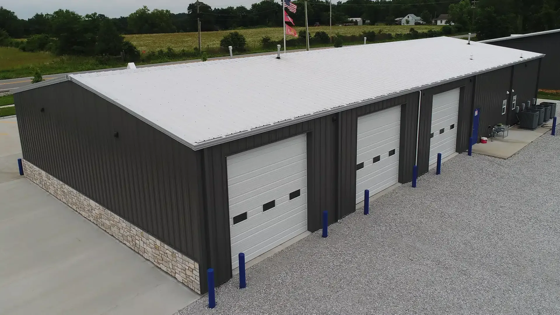 Metal building with three garage doors, gravel parking, and a white corrugated metal roof.