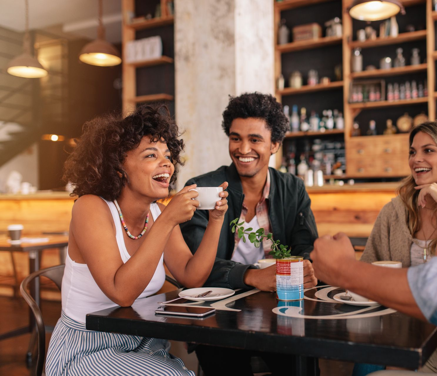 People laughing and talking around a table in a cafe, enjoying coffee and each other's company.