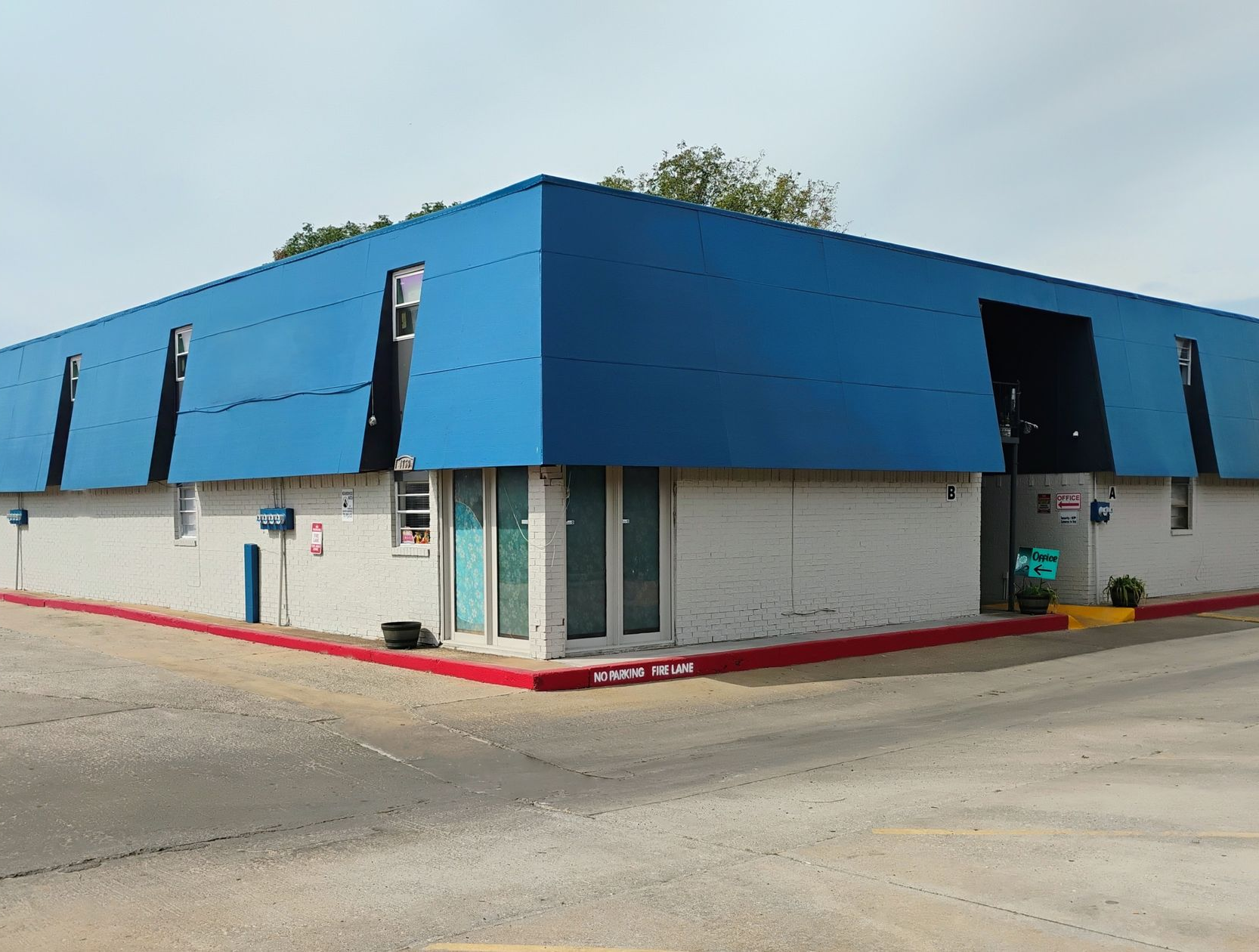 Blue-roofed, white-walled commercial building on a street corner, with red trim and windows.
