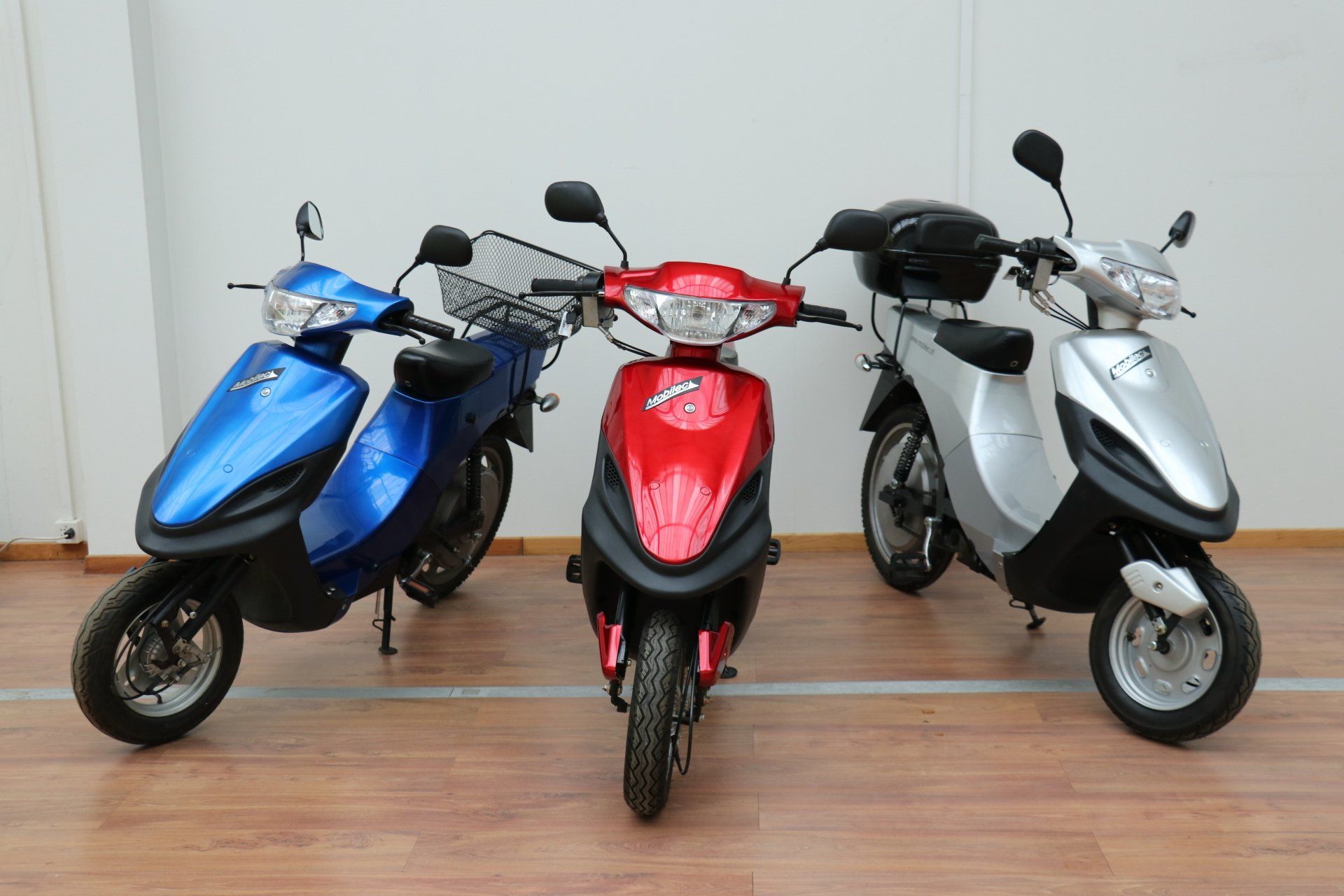 Trois scooters sont garés les uns à côté des autres sur un plancher en bois.
