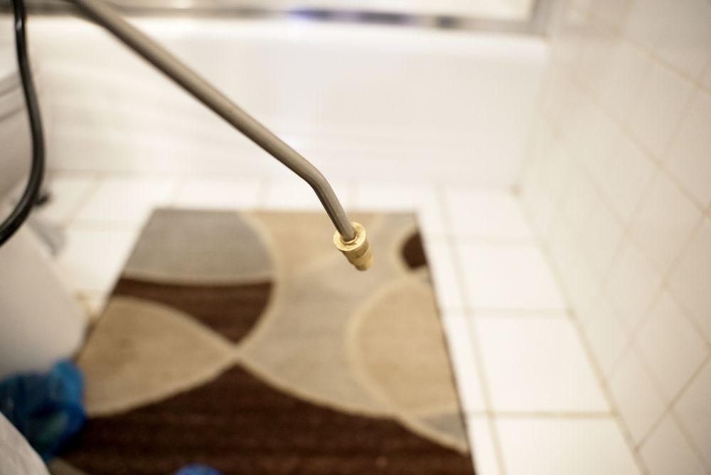 Close-up of a metal faucet spraying water into a tiled bathroom shower over a patterned rug.