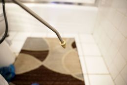 Close-up of a metal faucet spraying water into a tiled bathroom shower over a patterned rug.