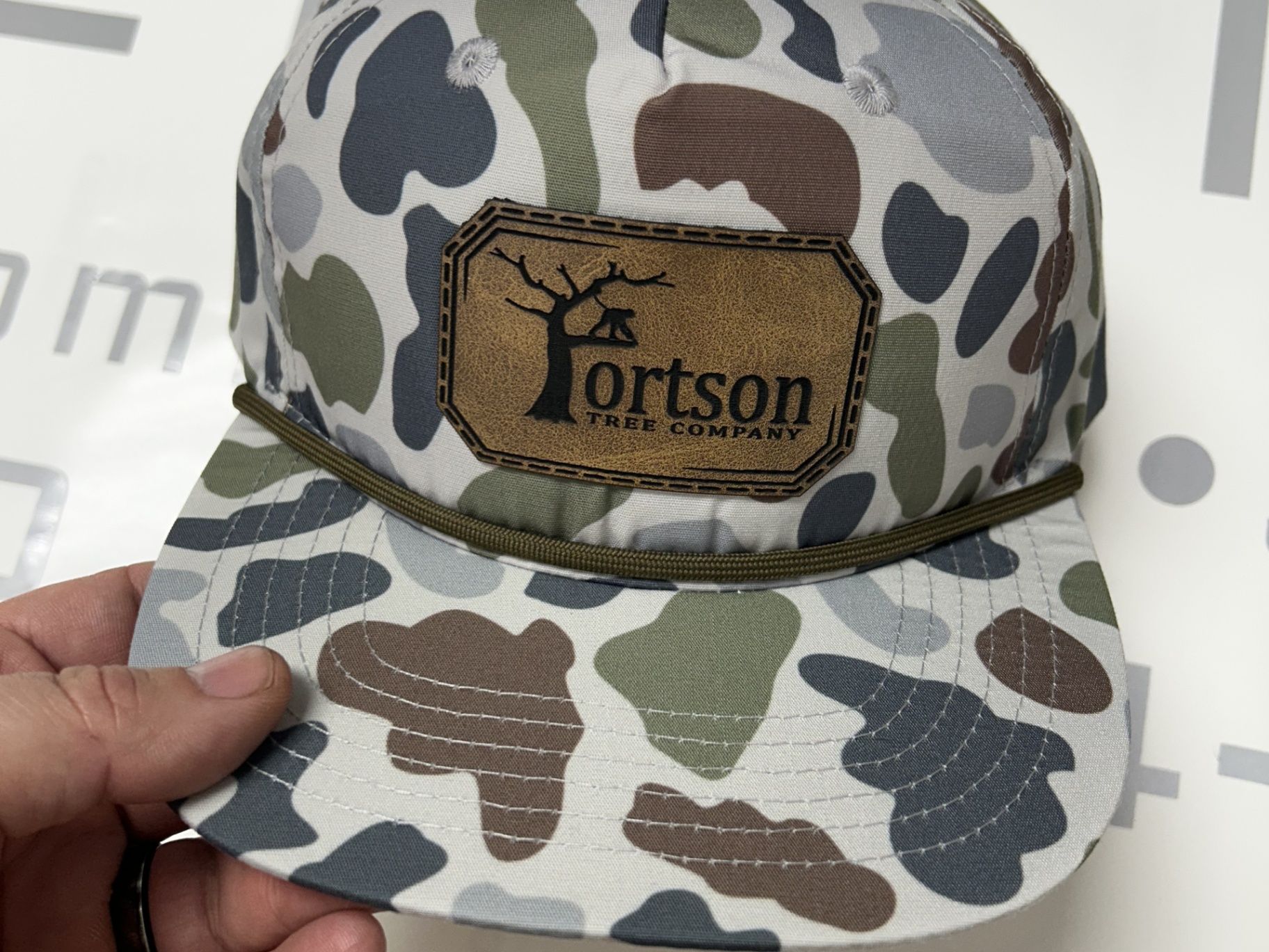 Camouflage hat with a brown patch that reads 