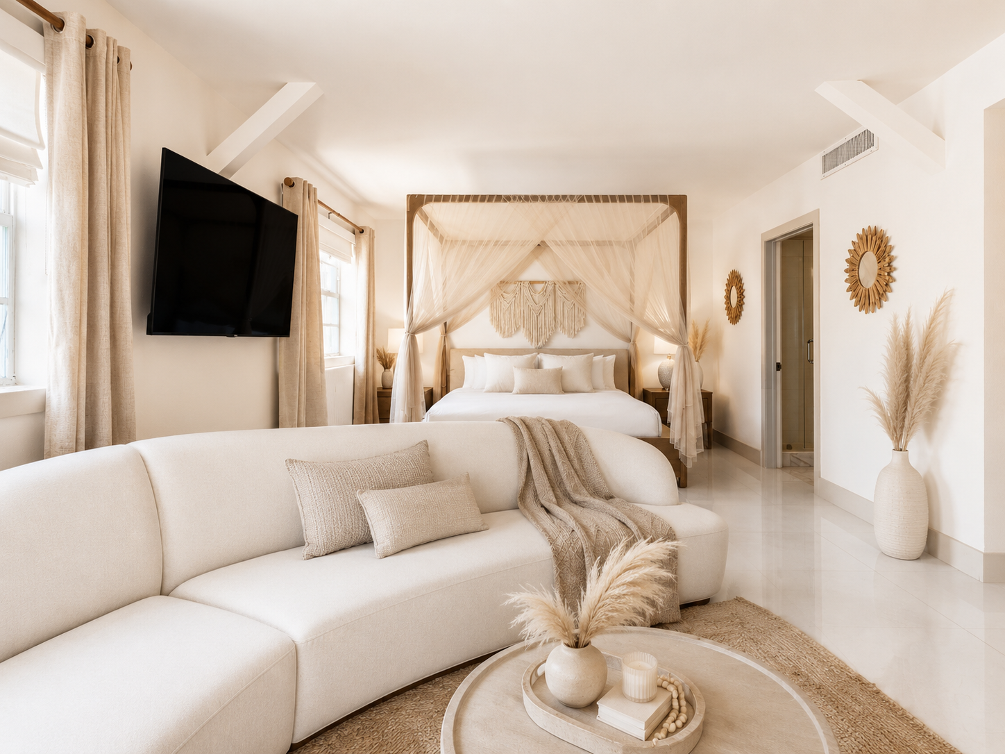 Minimalist cream bedroom with canopy bed, curved sofa, wall-mounted TV, and woven decor