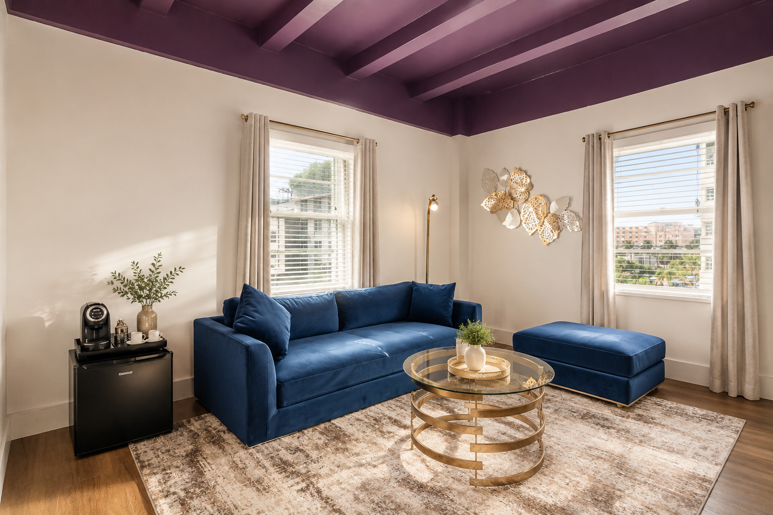 Modern living room with purple ceiling, blue sofa, gold coffee table, and two windows.