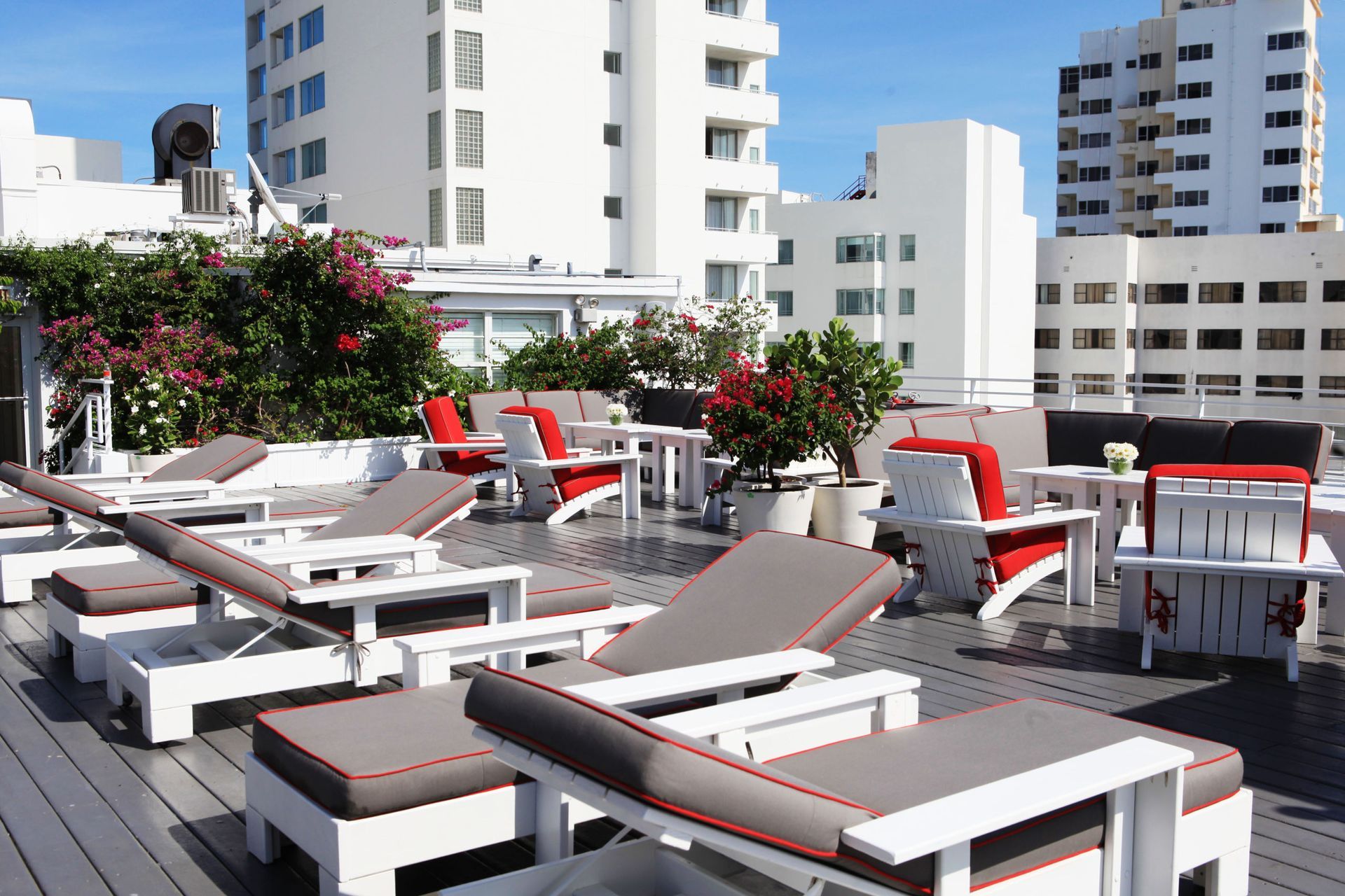 Rooftop terrace with lounge chairs, red cushions, and potted flowers overlooking city buildings