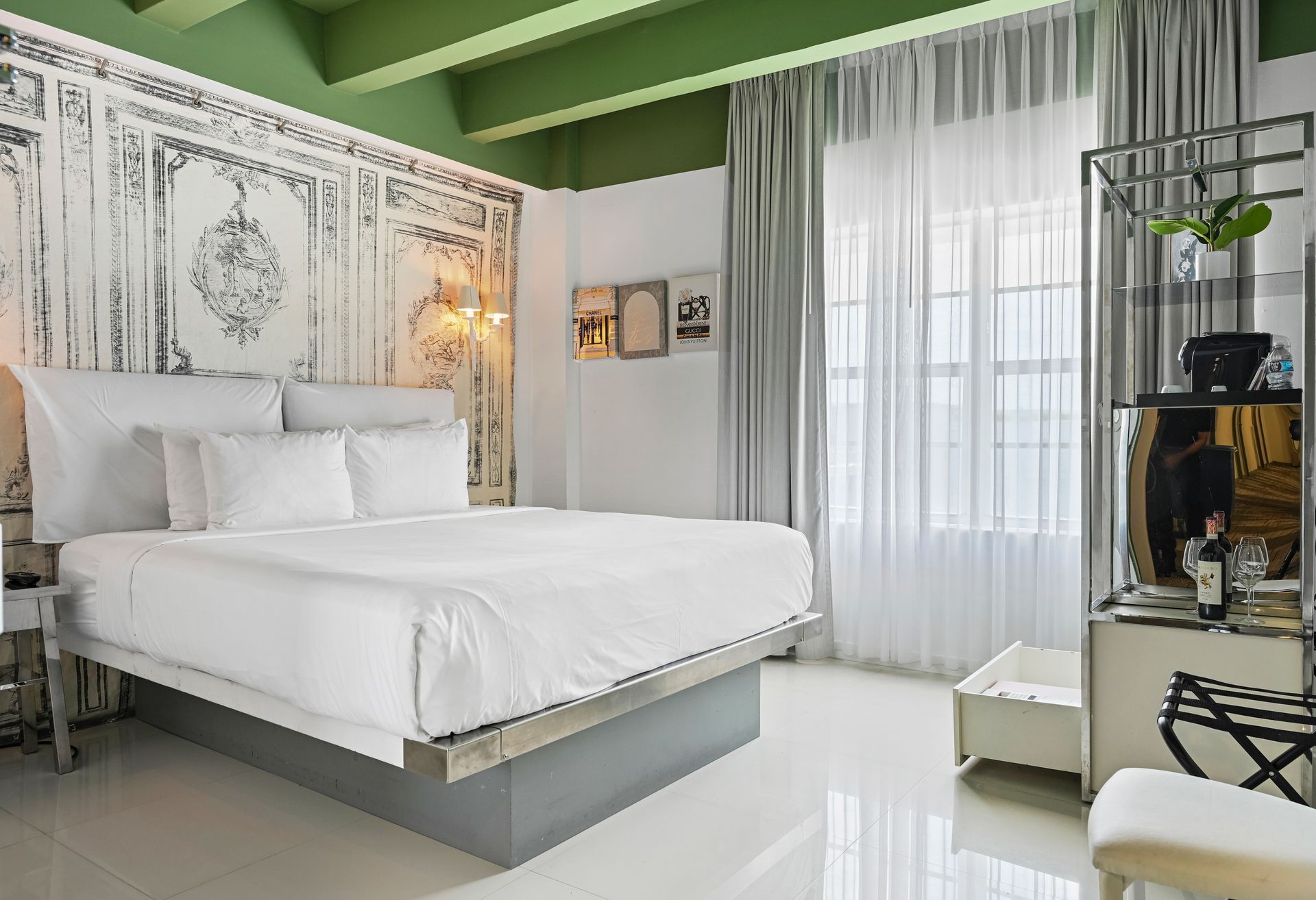 Modern bedroom with a made bed, green walls, and sliding doors to a patio with potted plants