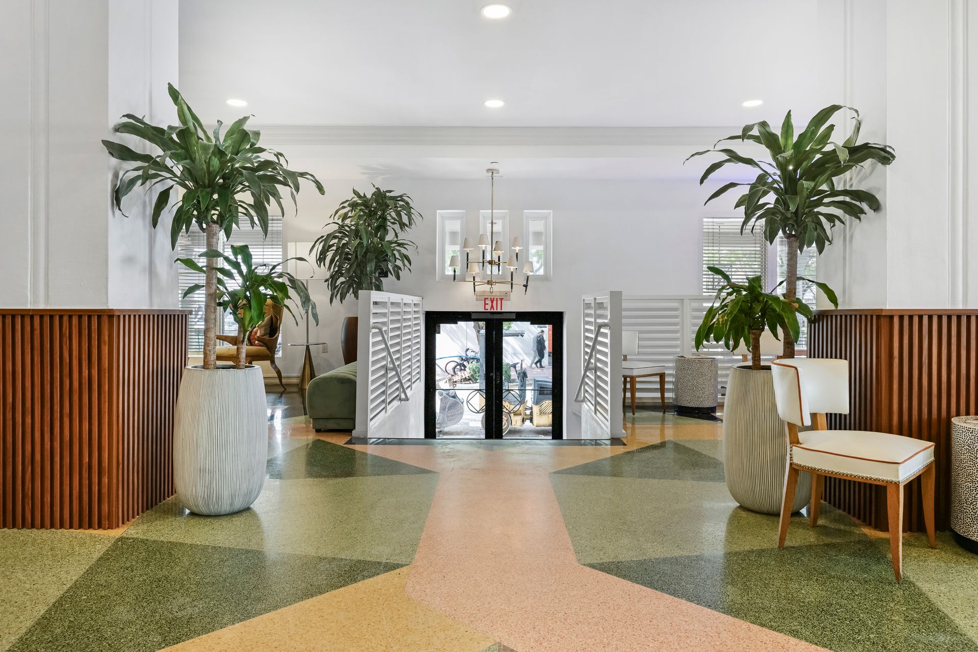 Bright, modern lobby with potted palms, wooden accents, and glass doors at the far end.