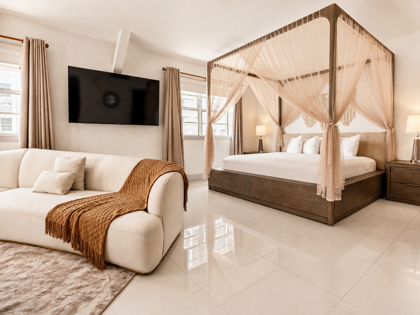 Modern bedroom with a canopy bed, beige sofa, wall-mounted TV, and glossy tile floor.