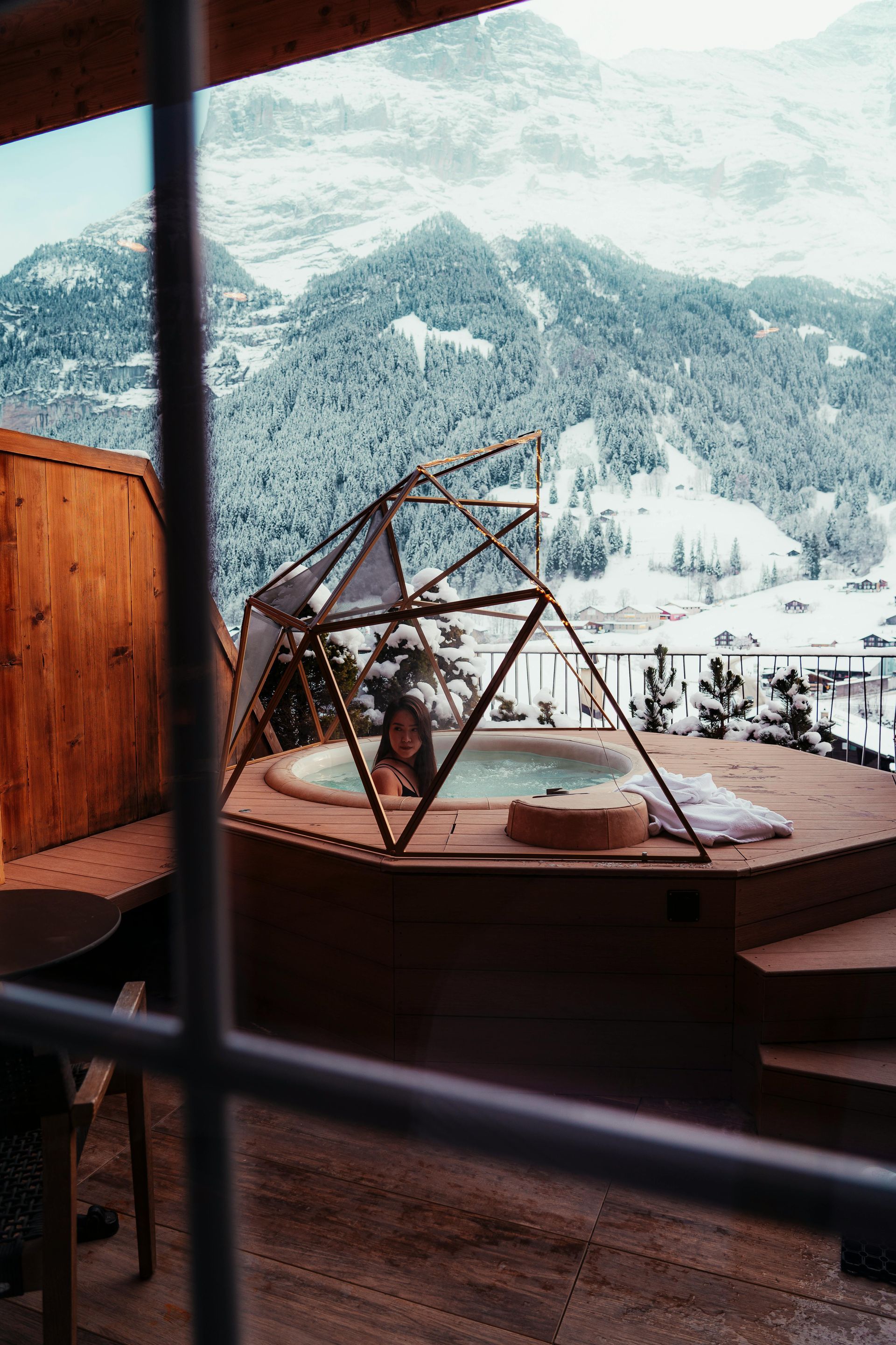 Hot tub on a snowy mountain balcony, with a small geodesic glass canopy and forested peaks beyond