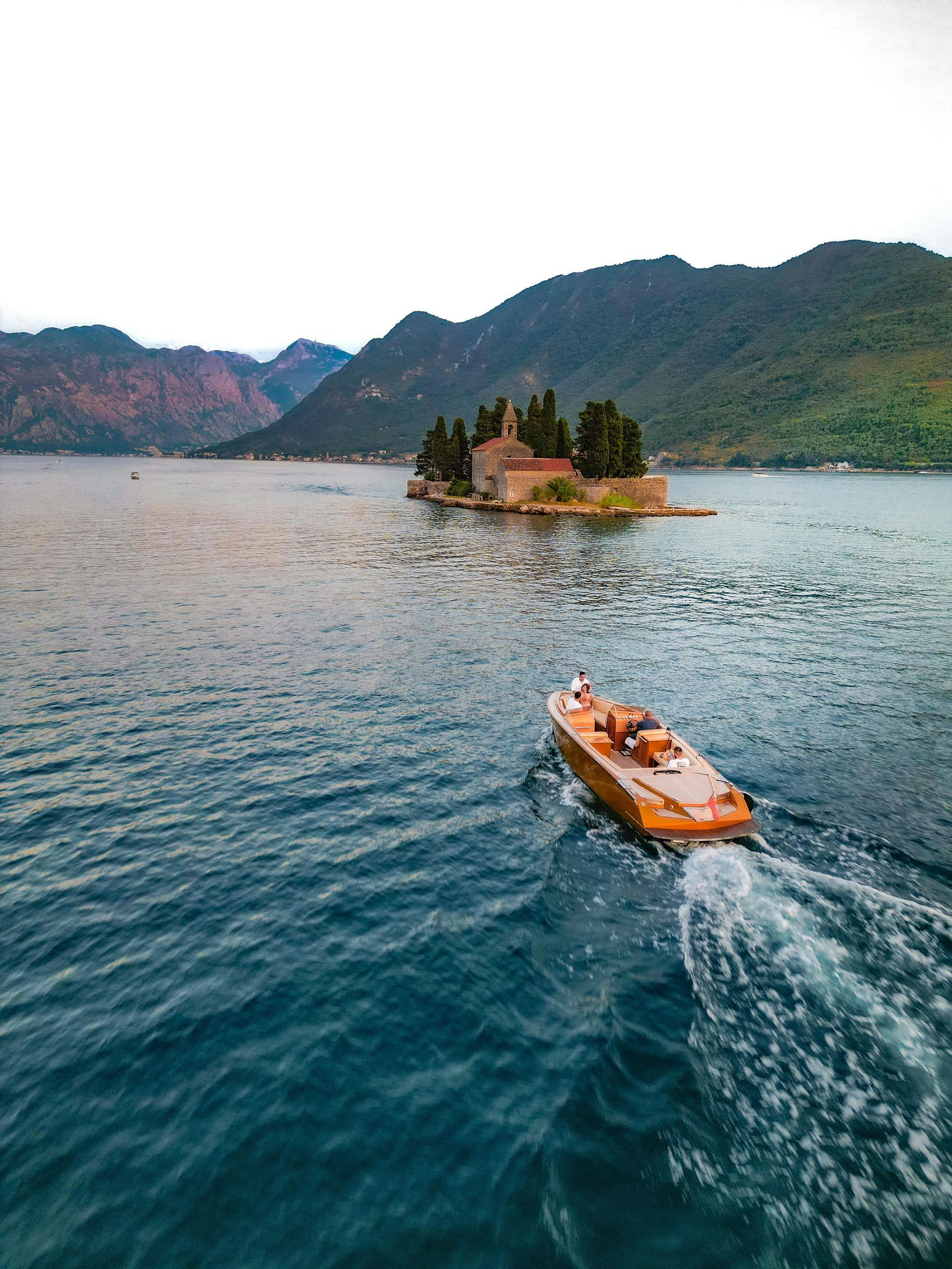 Orange boat on blue lake approaching a small island with a temple, backed by forested mountains.