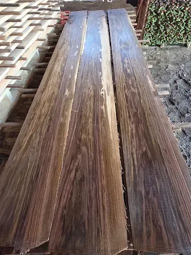 Long, dark-grained wooden planks laid out side-by-side in a lumber yard.