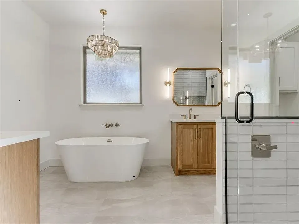 Bright, modern bathroom with freestanding tub, wooden vanity, and glass shower.