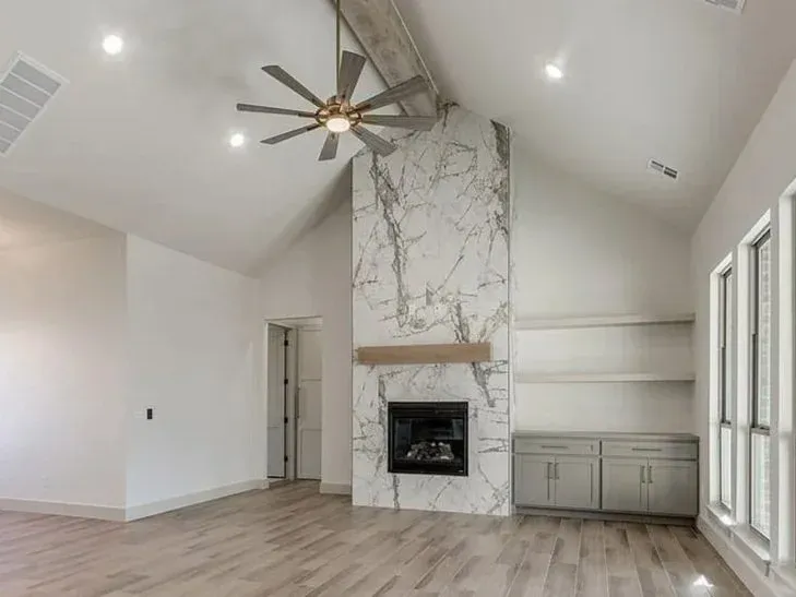 Modern living room with marble fireplace, light wood floors, and vaulted ceiling.