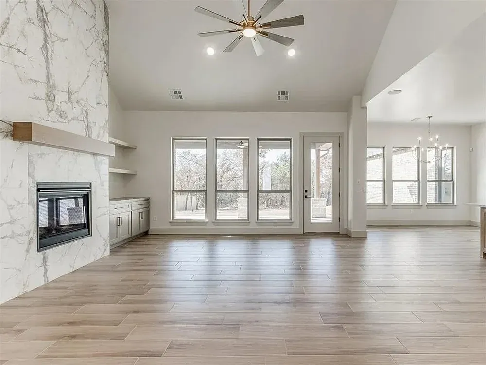 Empty living room with fireplace, large windows, and hardwood floors.