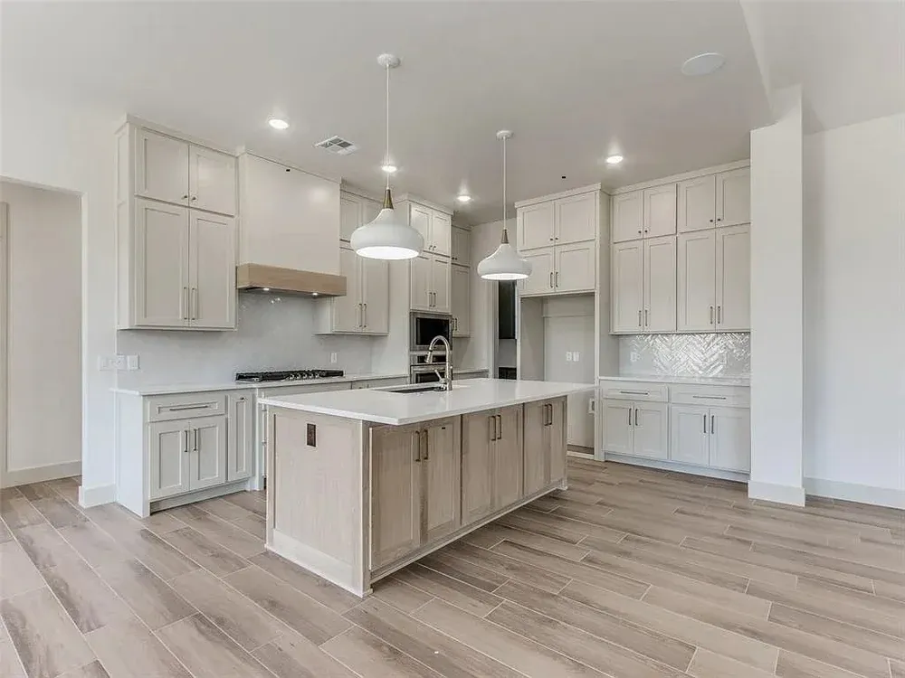 Spacious, light-filled kitchen with white cabinetry, central island, light wood floors, and pendant lighting.