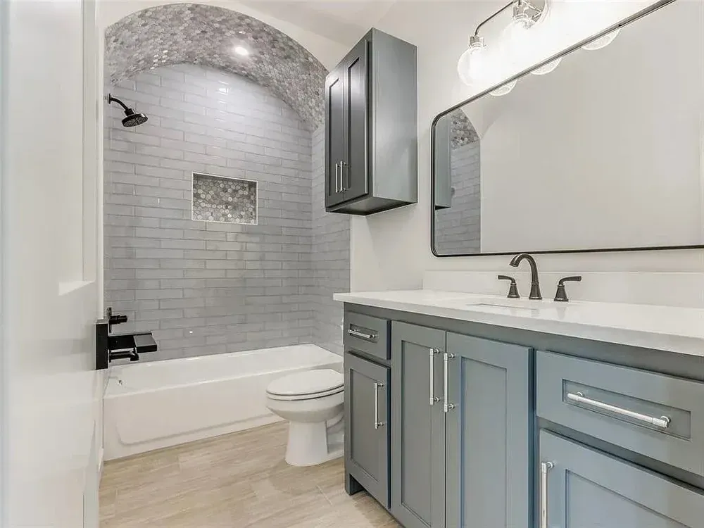 Bathroom with gray cabinets, white countertops, subway tile shower, and neutral-toned flooring.